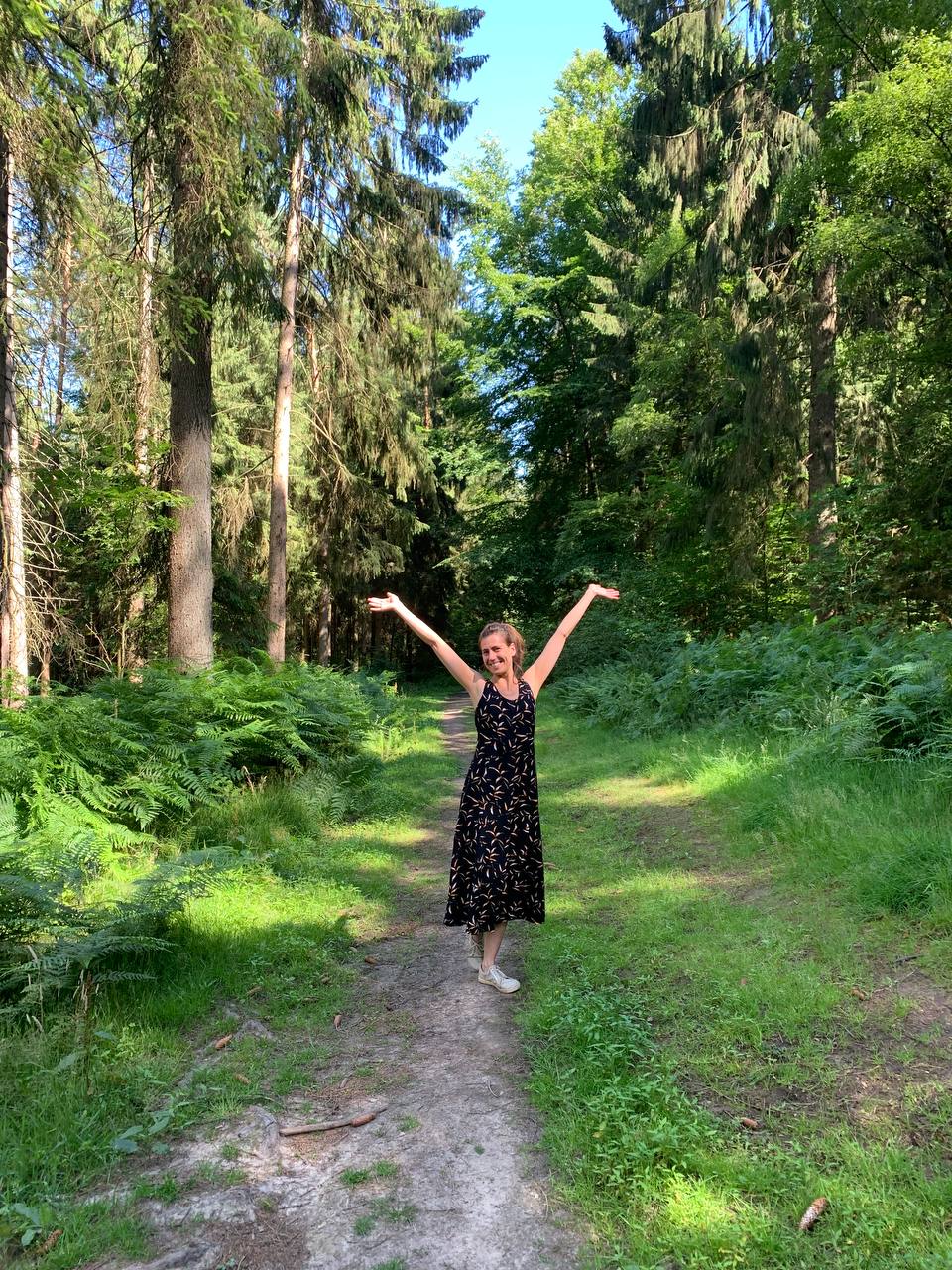 Frau steht freudig im Wald und wirft die Arme in die Luft.