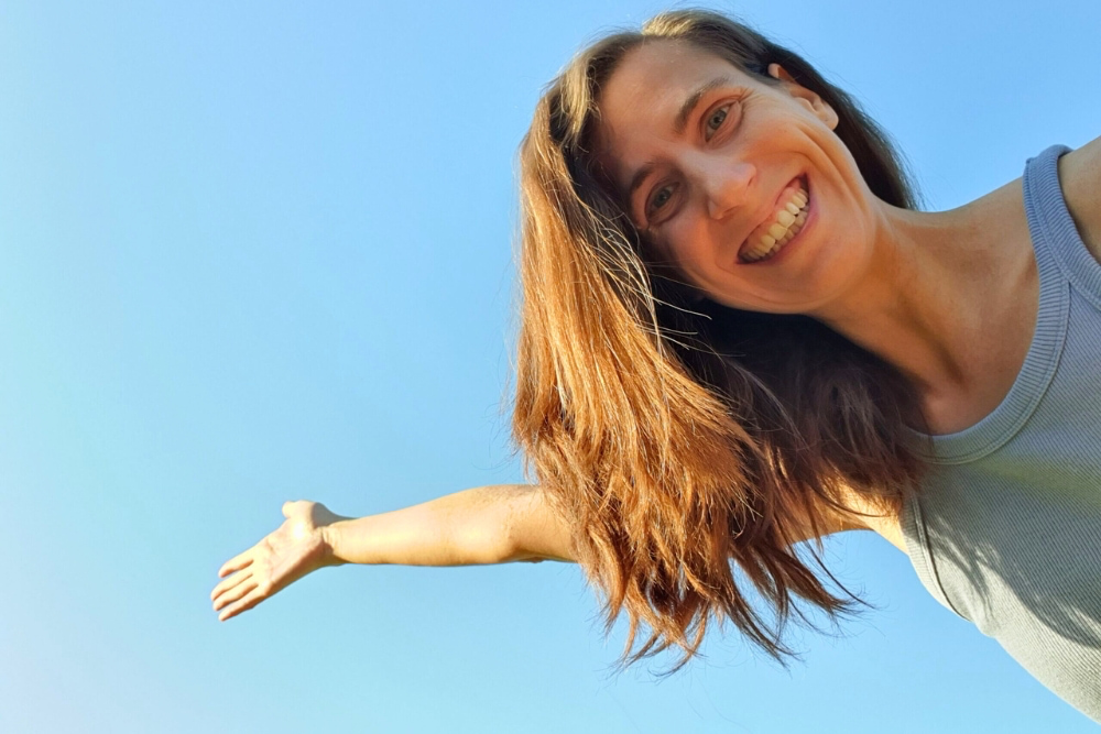 Catherina, Autorin des Blogs Wegweiser Neurodermitis, strahlt fröhlich bei blauem Himmel und Sonnenschein.