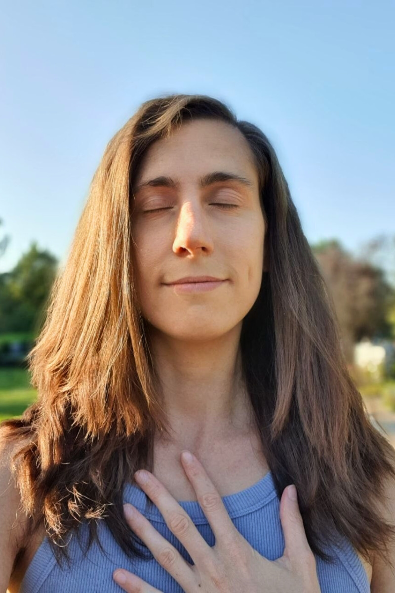 Catherina, Autorin des Blogs Wegweiser Neurodermitis, atmet meditativ mit geschlossenen Augen draußen bei Sonnenschein.