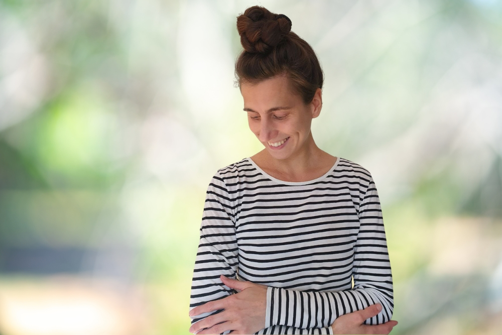 Catherina, Autorin des Blogs Wegweiser Neurodermitis, umfasst selbstliebend ihre Arme und schaut zufrieden hinunter. Symbolisch für angenehme Kleidung auf der Haut.