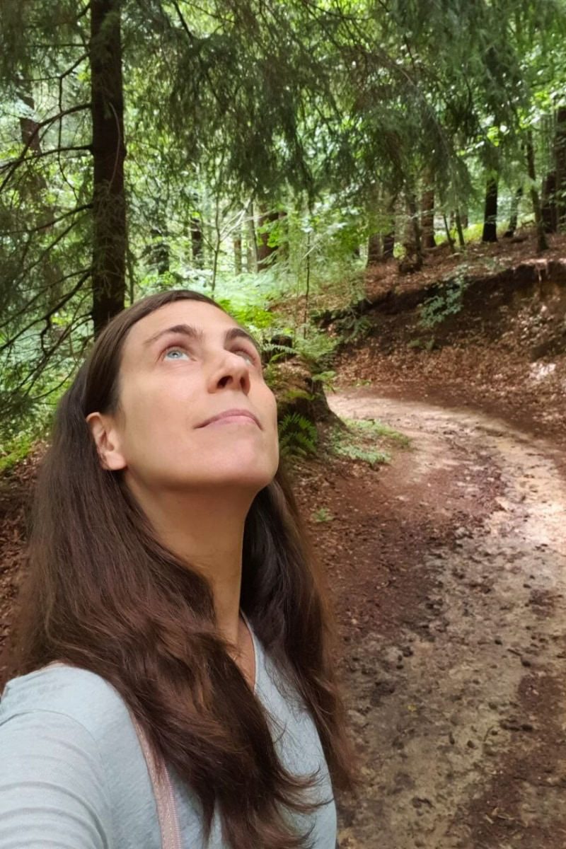 Catherina, Autorin des Blogs Wegweiser Neurodermitis, blickt auf Waldweg nach oben in die Baumkronen. Symbolisch für mehr Freiheit durch verbesserte Atmung.