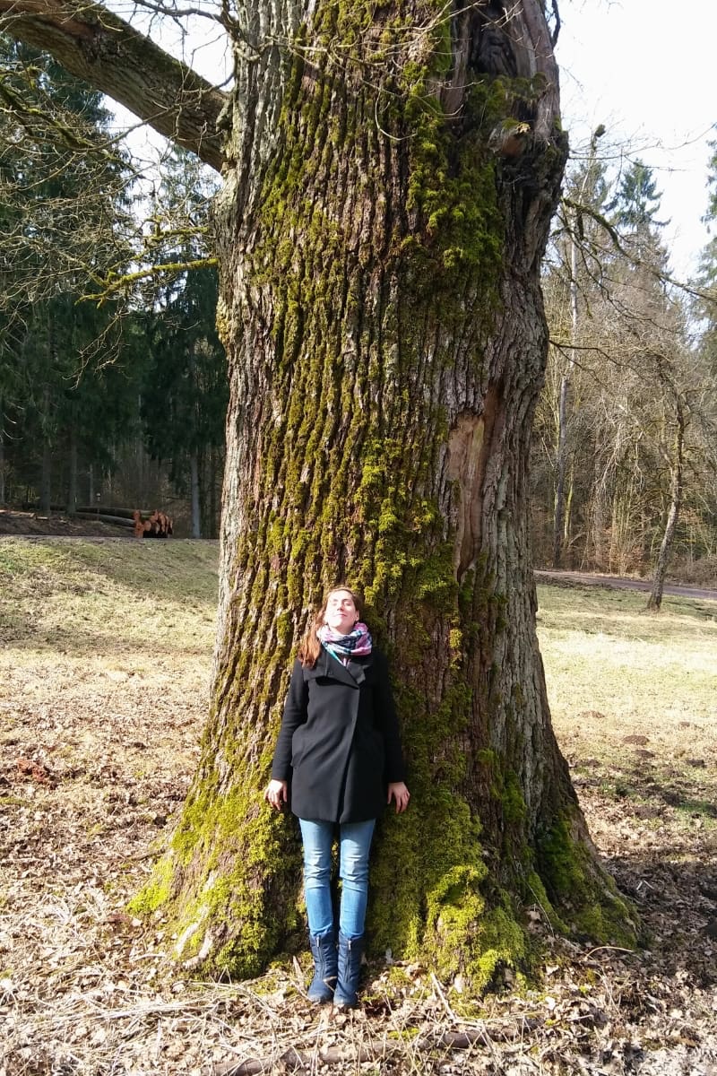 Frau, die sich mit geschlossenen Augen an einer alten Eiche anlehnt. Symbolisch für die Kraft des Atems.